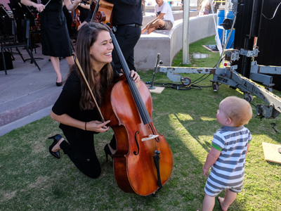 music student holding stringed instrument, engaging with an infant. Photo Credit: Rich Williams
