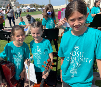 three young music students, wearing matching teal shirts and holding their stringed instruments